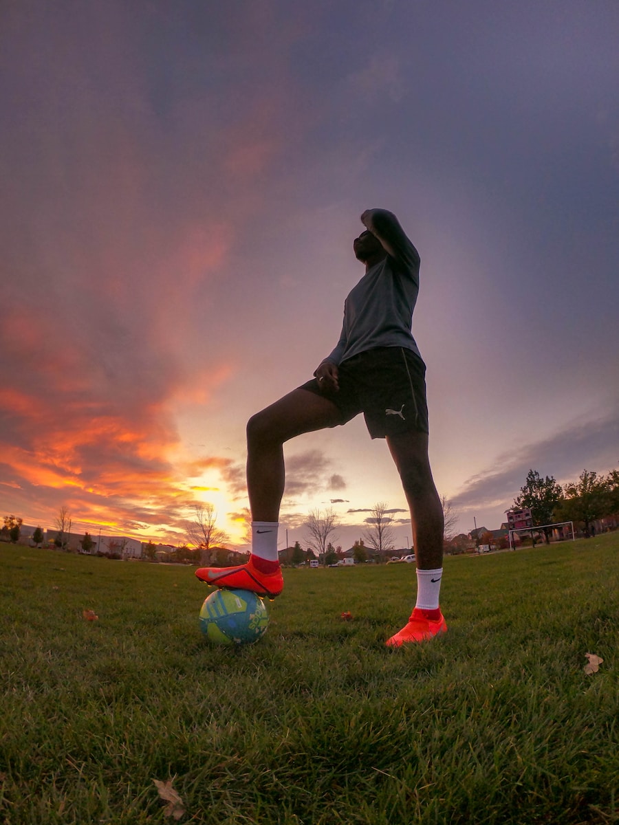 man in black hoodie playing soccer on green grass field during sunset
